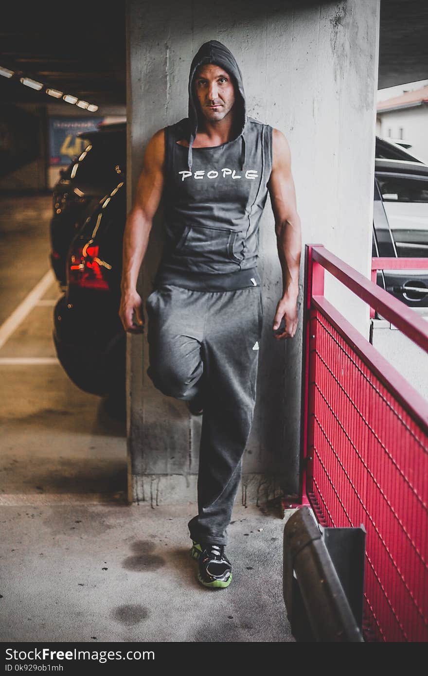 Man Wearing Black Hooded Top and Black Adidas Pants Leaning on Gray Wall