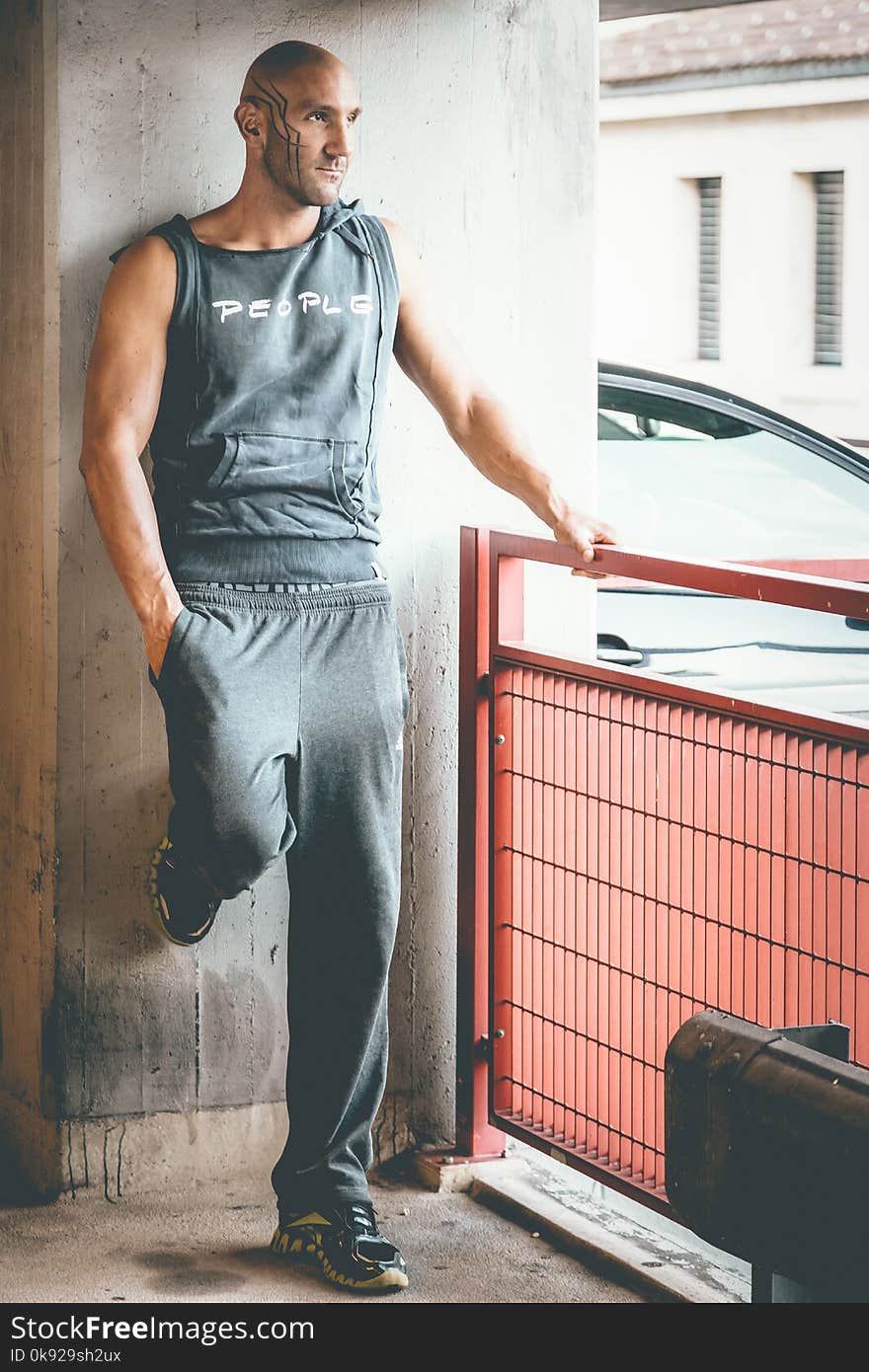 Man Wearing Gray Tank Top and Track Pants Leaning on Wall