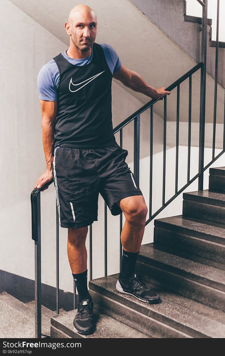 Man Wearing Black Nike Tank Top Placing His Hands on Black Stair Handrail