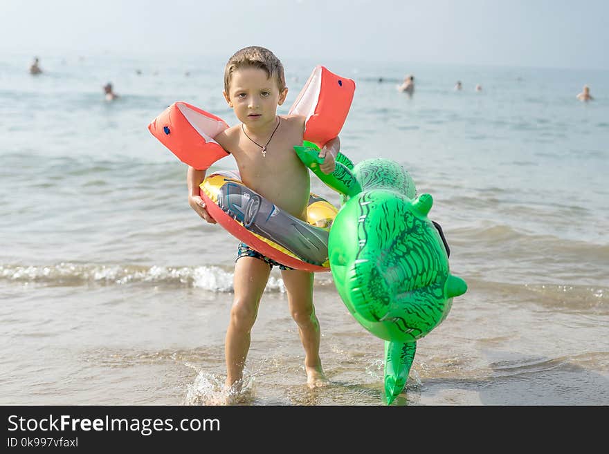 Happy smiling little boy run play with waves on beach. Italy. Summer