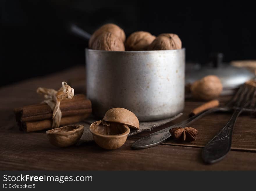 Walnuts in a metal bowl, dark background. Walnut shell and cinnamon on the wooden table.