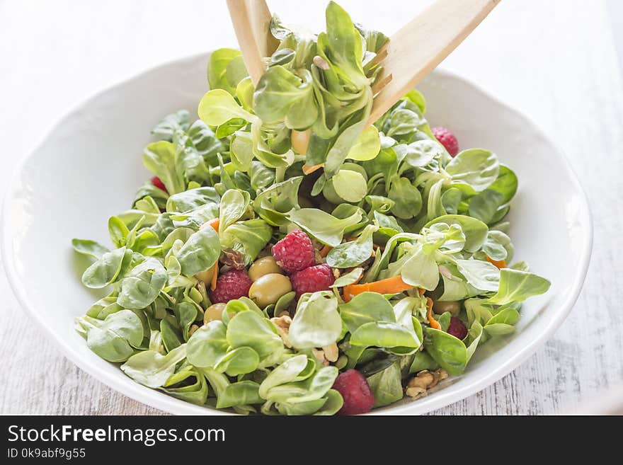 Salad of canons, raspberries, raisins, olives, nuts, carrots and pips. Wooden spoon and fork. Salad of canons, raspberries, raisins, olives, nuts, carrots and pips. Wooden spoon and fork.