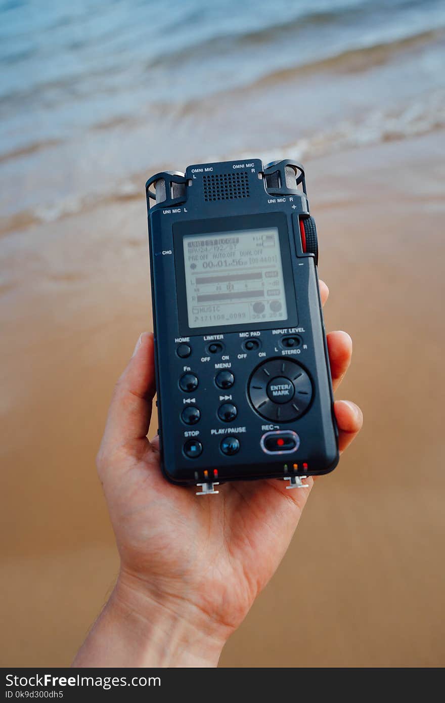 Portable audio recorder in hand recording ambient sounds of sea, closeup view