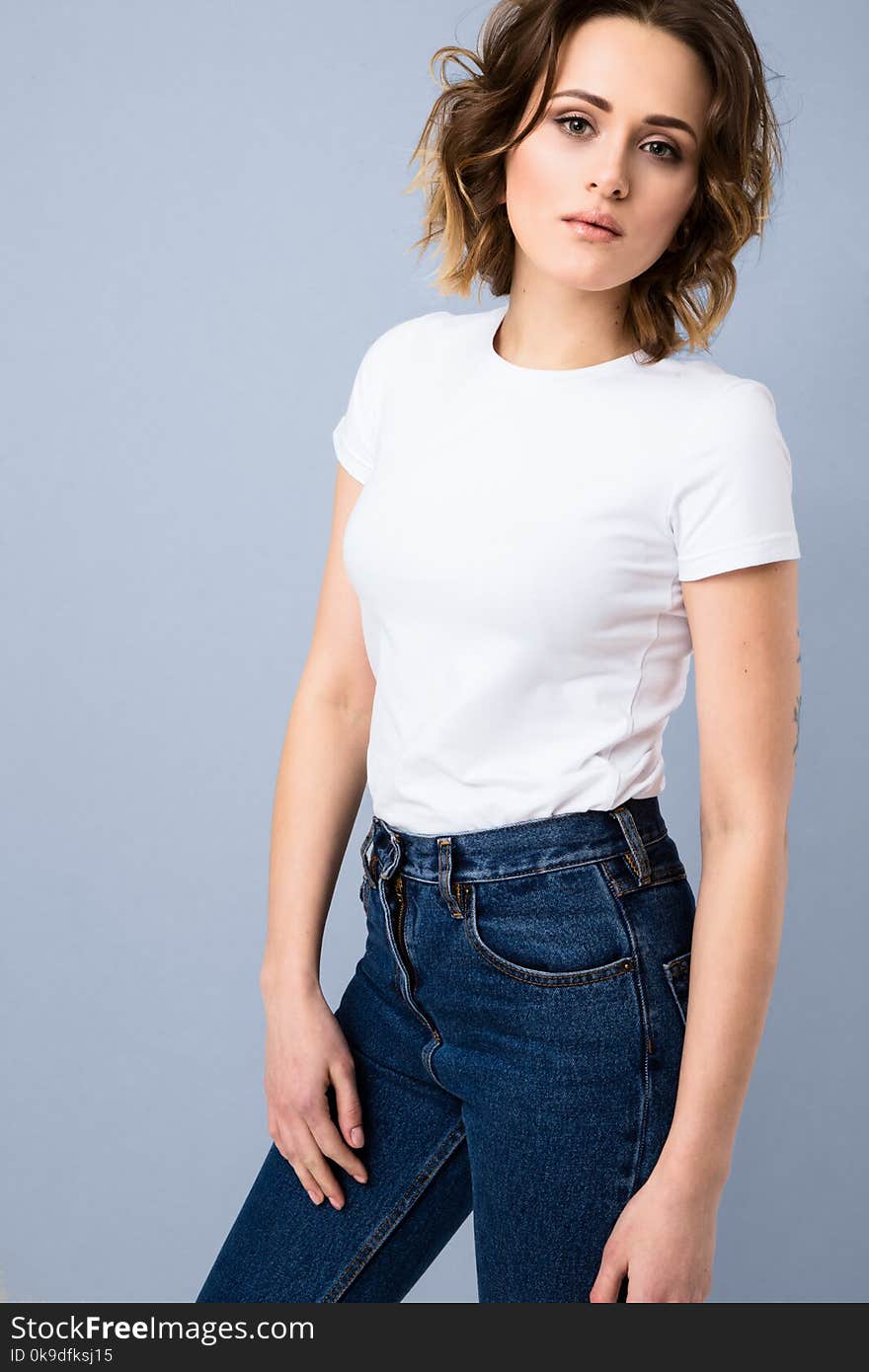 Portrait of stylish young girl in basic white t-shirt and high waisted blue jeans posing in studio on grey background