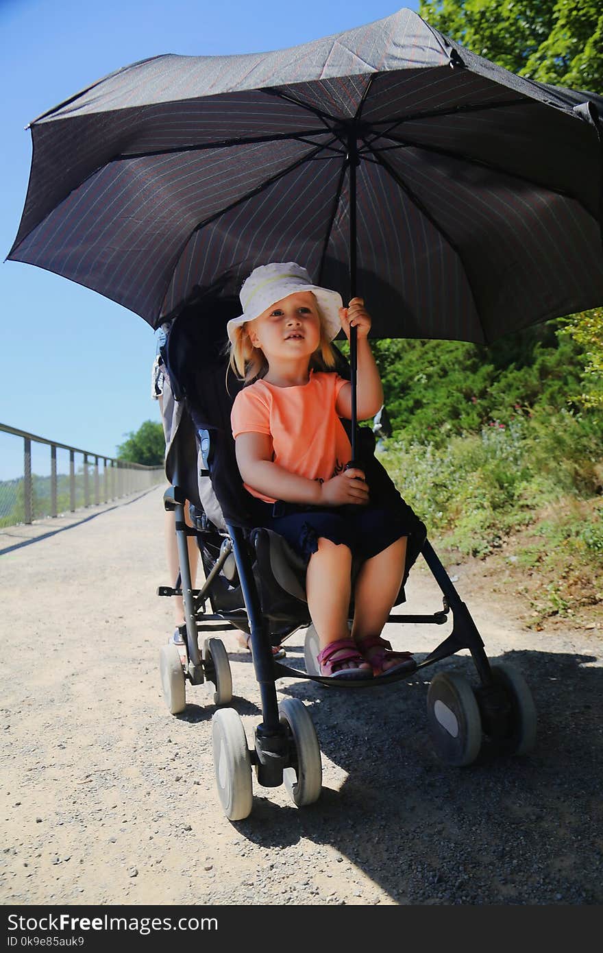 Little girl sitting in stroller. Child protected from sun by big umbrella. Kid Heatstroke prevention on sunny day in summer