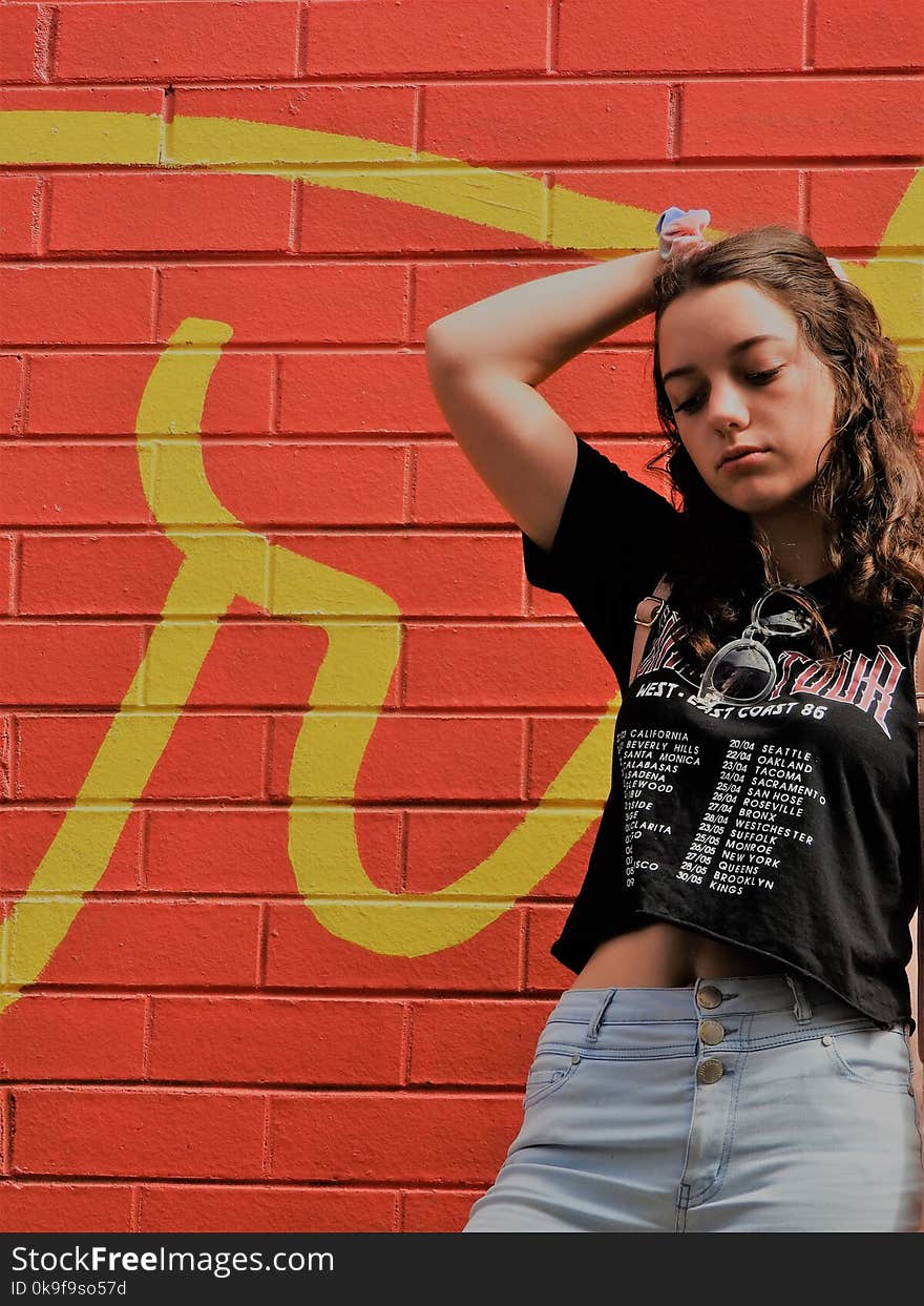 Woman In Black Shirt And Blue Bottoms Standing Near Red Wall