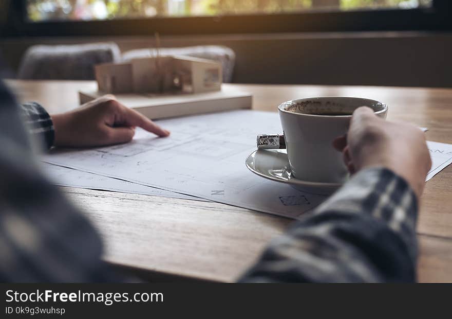 An architect working on an architecture model with shop drawing paper while drinking coffee in office