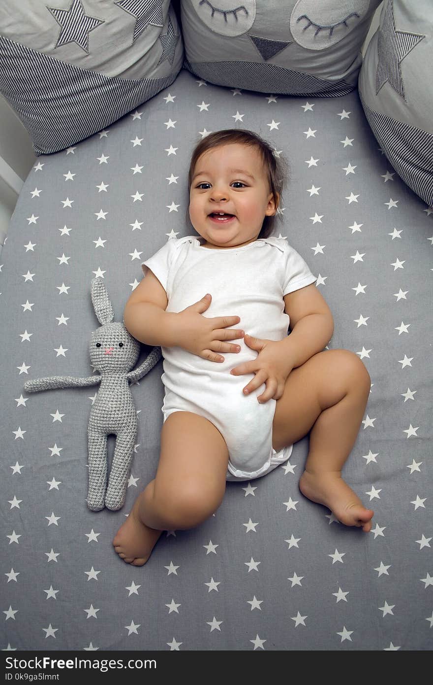 One year old baby boy lying in a round bed with a knitted rabbit toy