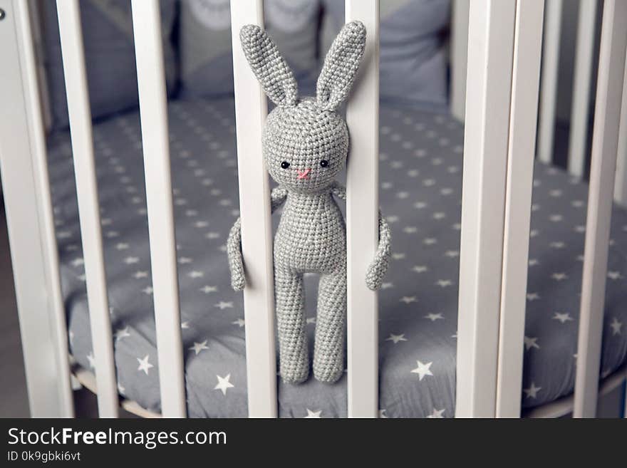 Grey knitted rabbit sitting behind the partitions