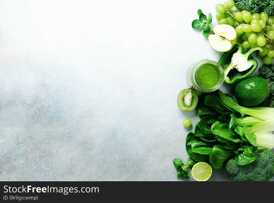 Green smoothie in glass jar with fresh organic green vegetables and fruits on grey background. Spring diet, healthy raw