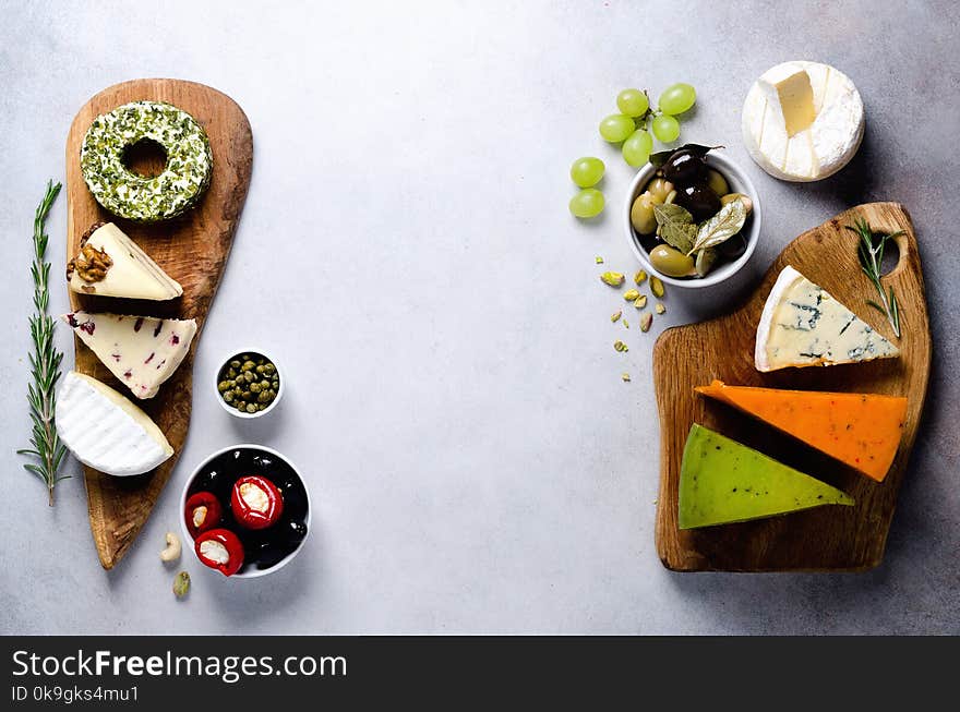 Assortment of hard, semi-soft and soft cheeses with olives, grissini bread sticks, capers, grape, on grey concrete