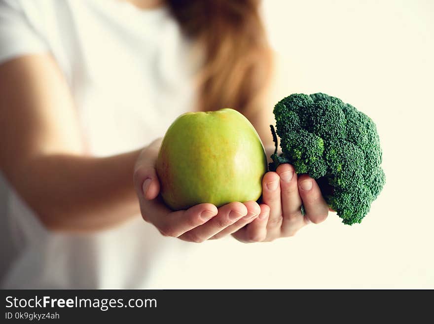 Woman in white T-shirt holding geen apple and broccoli in her hands. Copy space. Clean detox eating, vegetarian, vegan, raw concept.