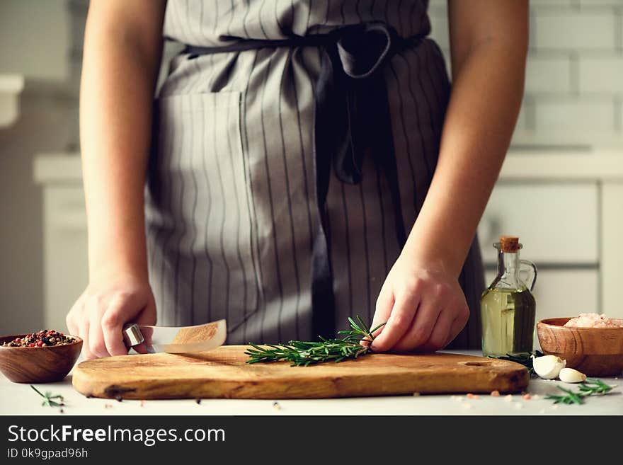 Woman hands cutting fresh green rosemary on wood chopping board in white kitchen, interior. Copy space. Homemade food conceplt, healthy recipe.