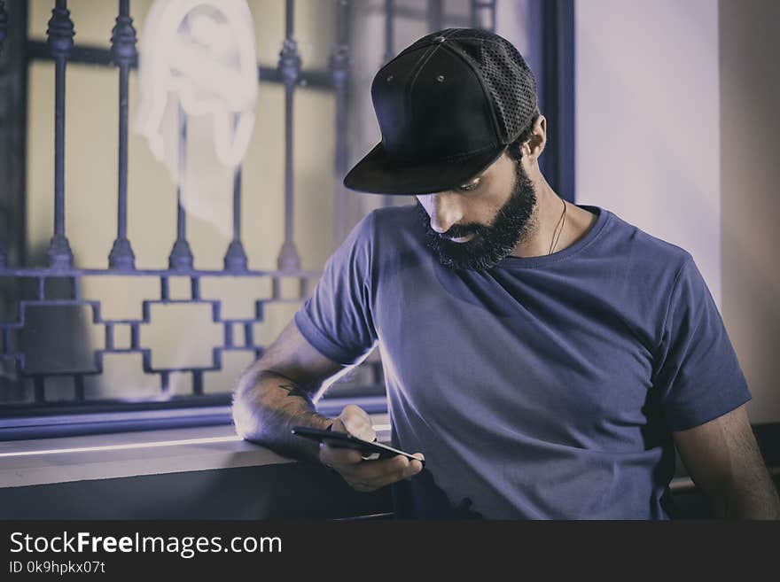 Young Bearded Man Sitting In Cafe And Using Smartphone For Texting Message. Horizontal. Blurred Background.