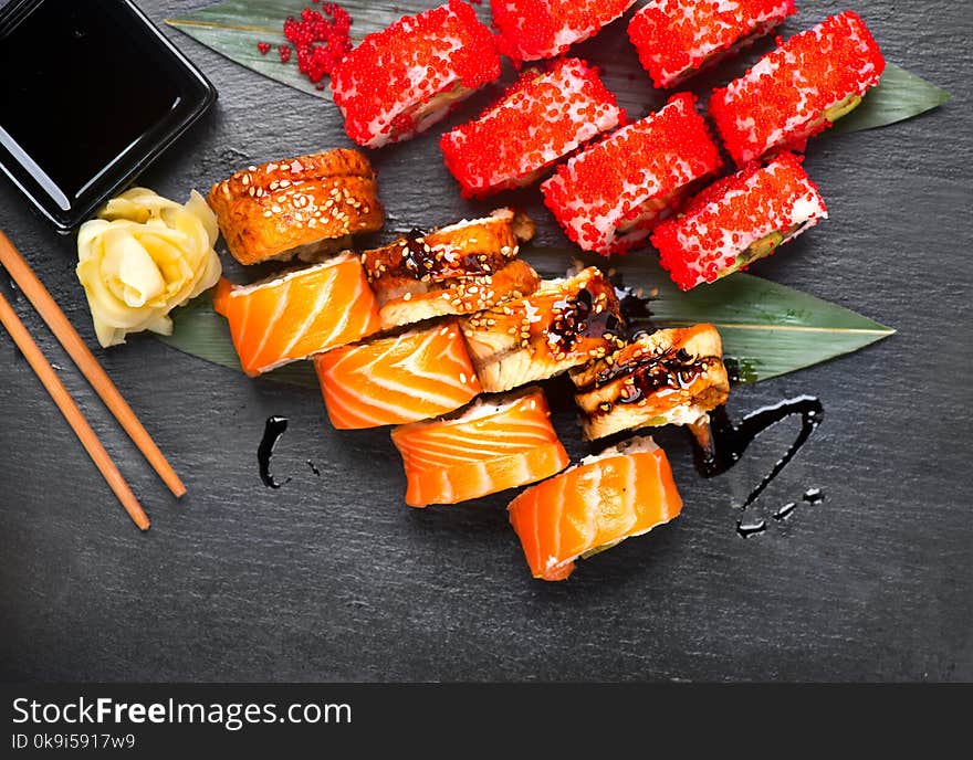 Sushi rolls closeup. Japanese food in restaurant. Roll with salmon, eel, vegetables and flying fish caviar on black slate background