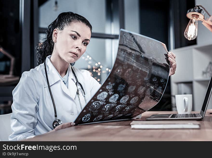 First results. Serious busy concentrated medic sitting in the her cabinet holding and overlooking x-ray scan. First results. Serious busy concentrated medic sitting in the her cabinet holding and overlooking x-ray scan.