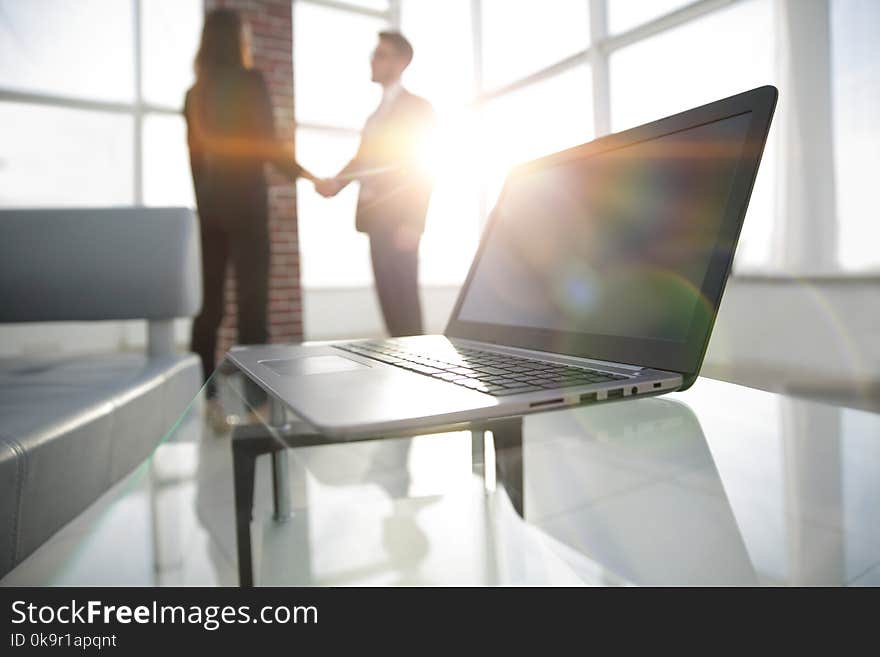 Laptop computer with folder on desk,two businesspeople standing in the background. Laptop computer with folder on desk,two businesspeople standing in the background