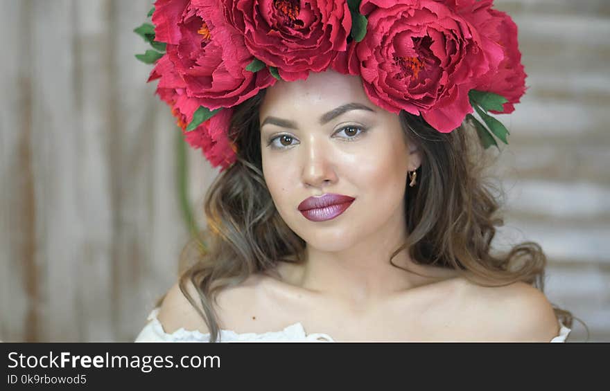 Girl posing in front of camera. young woman in a wreath of scarlet peonies on her head, dark long curly hair descends on the shallow shoulders. slow motion