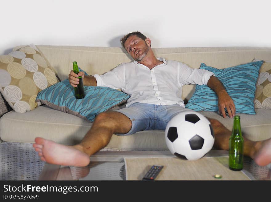 Young wasted soccer supporter man lying on home sofa couch sleep