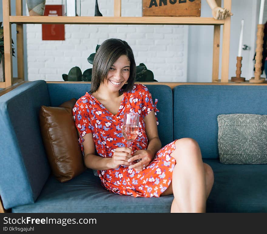 Woman Sitting at Sofa Wearing Red and Multicolored Floral Dress White Holding Glass