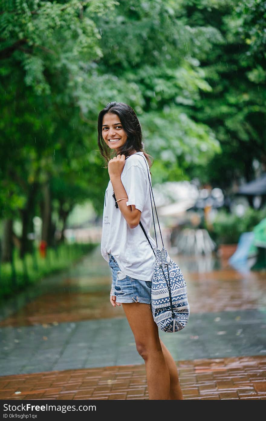 Shallow Focus Photography of Woman in White Shirt and Blue Denim Shorts on Street Near Green Trees