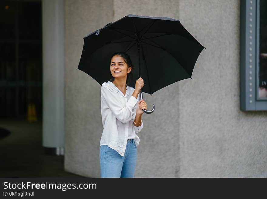 Photo of Woman Wearing White Long-sleeved Shirt and Blue Jeans Holding Black Umbrella