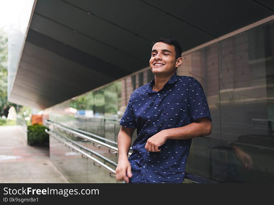 Man in Blue Button-up Shirt Standing Beside Glass Wall