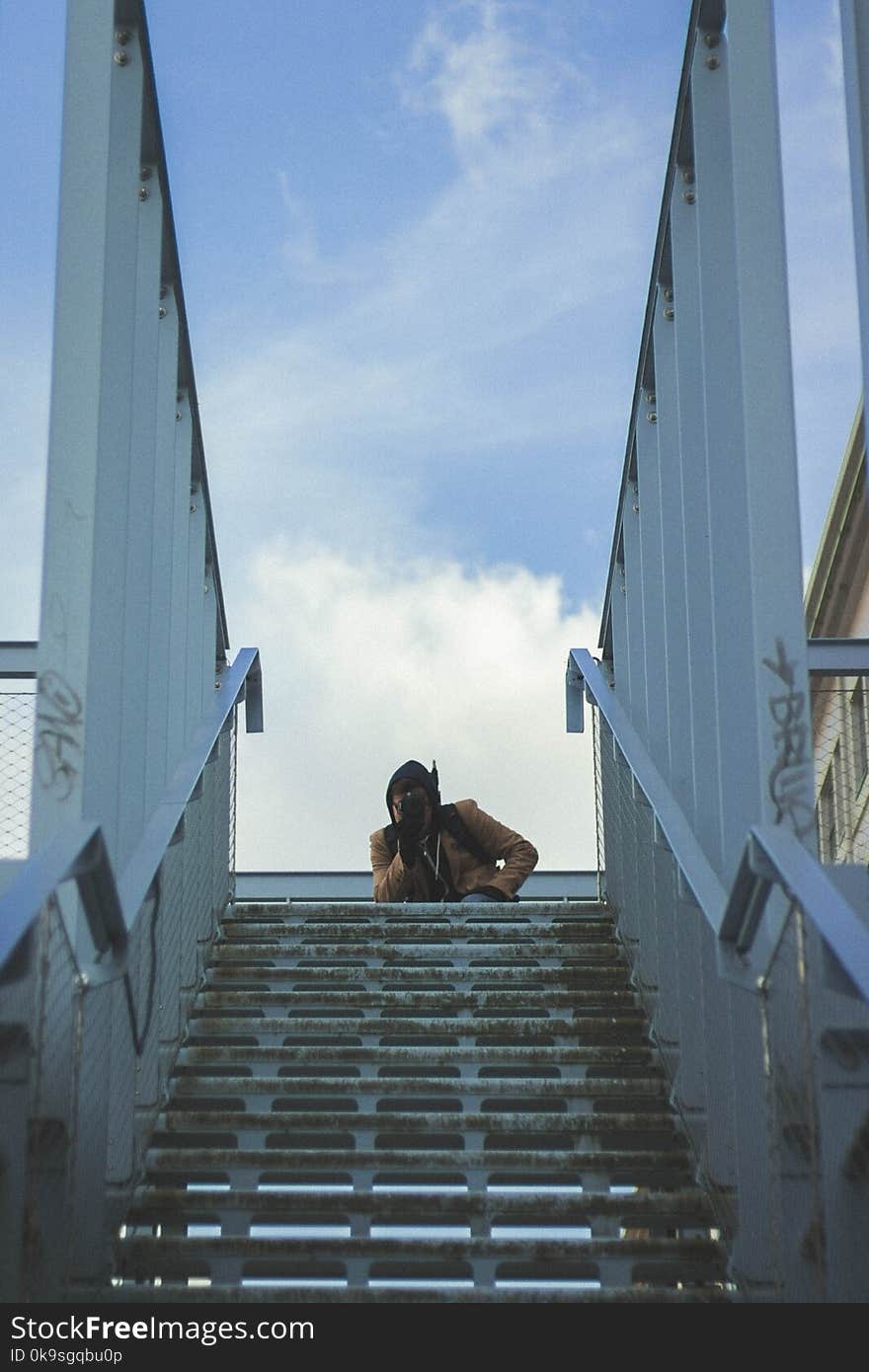 Person in Brown Coat on Bridge Under Cloudy Blue Sky