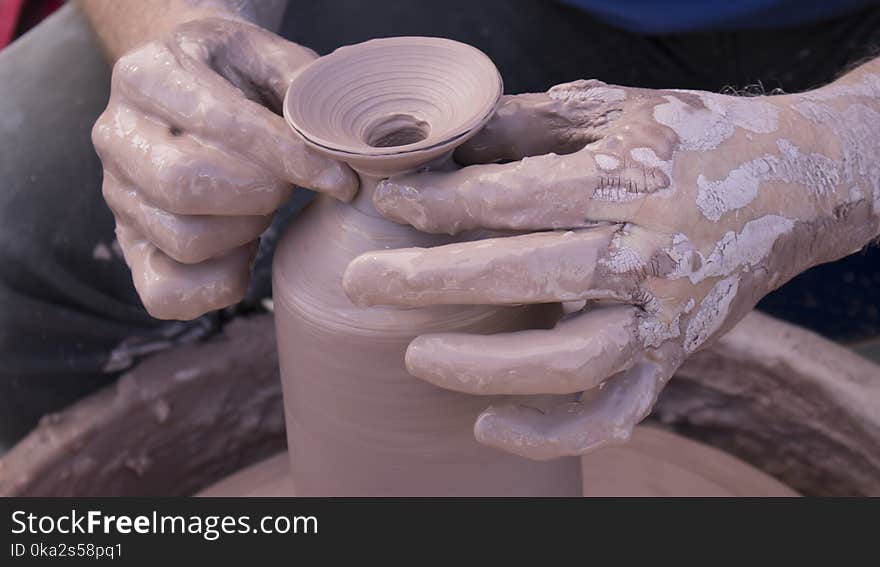 A Potters hands covered in clay forming a pot on a wheel close up