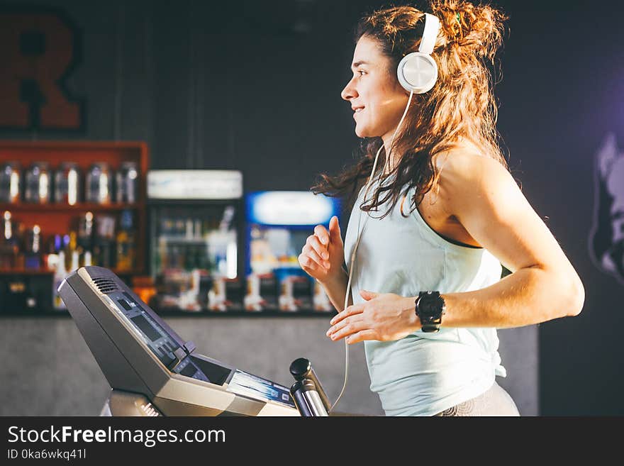 Theme is sport and music. A beautiful inflated woman runs in the gym on a treadmill. On her head are big white headphones, the girl listens to music during a cardio workout for weight loss.