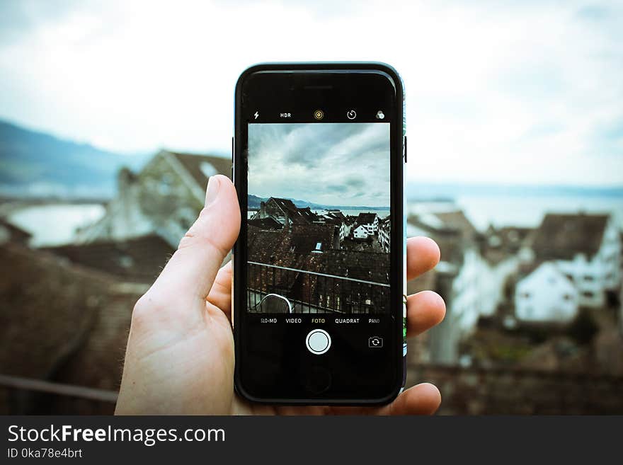 Person Holding Black Smartphone Taking a Picture of Brown House at Daytime