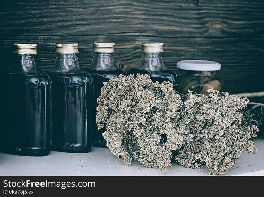 Four Clear Glass Bottles With Black Liquid Near Brown Flower Bouquet