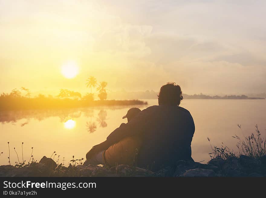 Two People On Grass Beside Body Of Water During Golden Hour