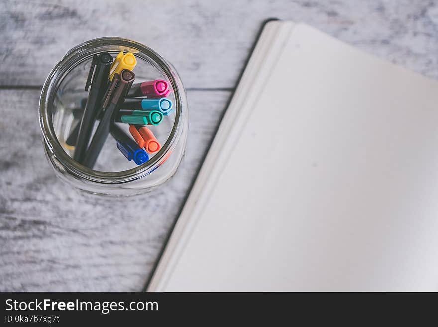 Clear Glass Jar Filled of Coloring Pens Beside of White Sketch Pad