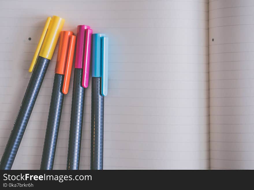 Yellow, Orange, Pink, and Blue Coloring Pens on White Notebook