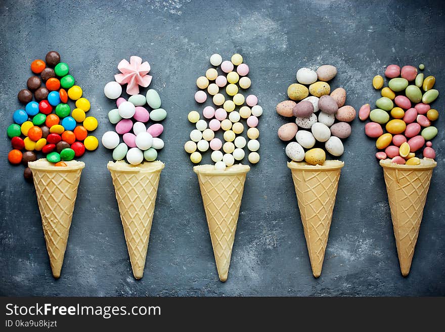 Candy in waffle cones on dark background. Flat lay, top view