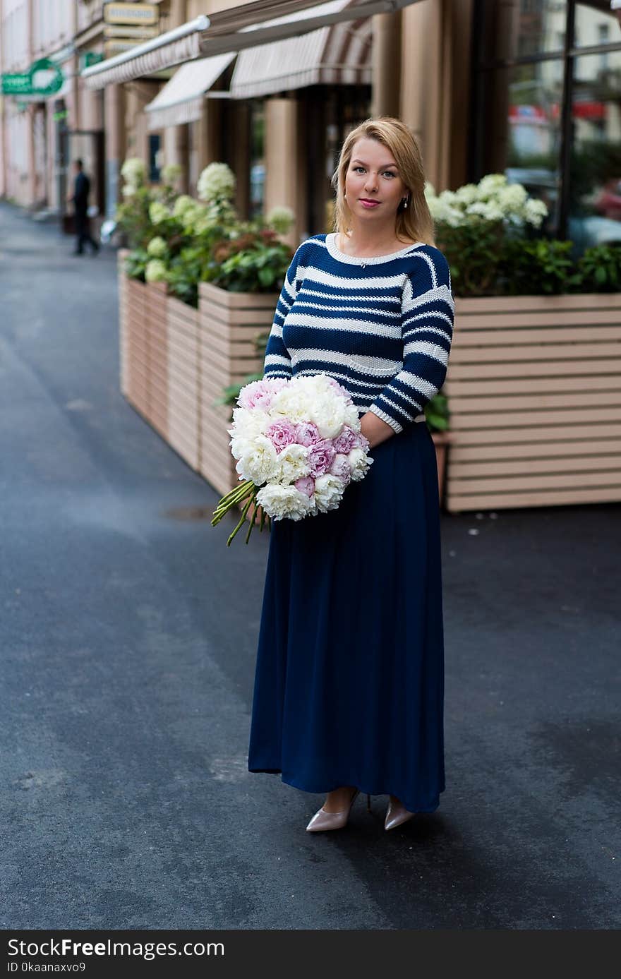 Young blonde woman in blue dress with peonies bouquet