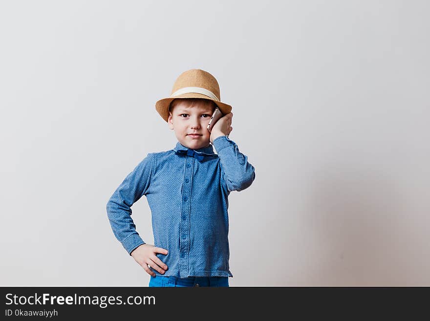 Little boy in blue shirt in hat talking on phone on white background