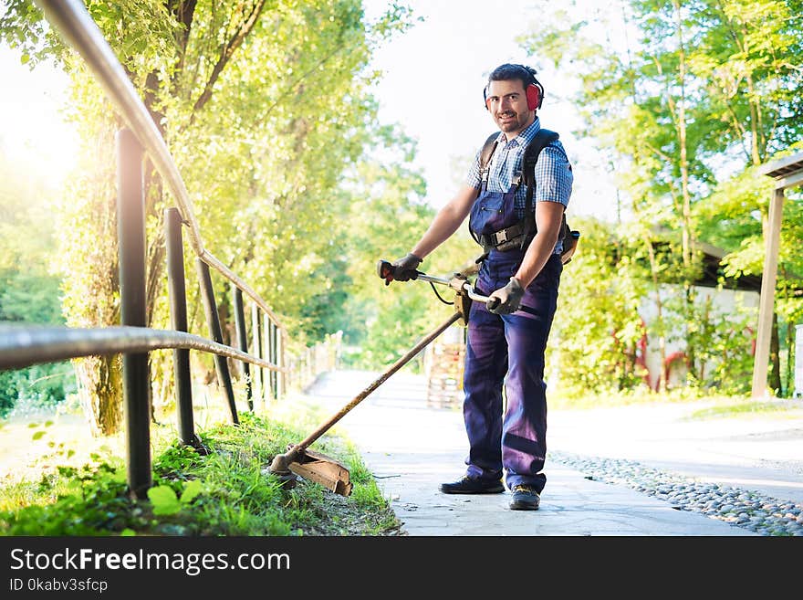 Man wearing ear protectors mowing grass in the backyard with petrol hedge trimmer. Man wearing ear protectors mowing grass in the backyard with petrol hedge trimmer