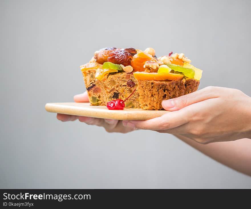 Female Hand Holding A Loaf Of Fruit Cake On Wooden Plate