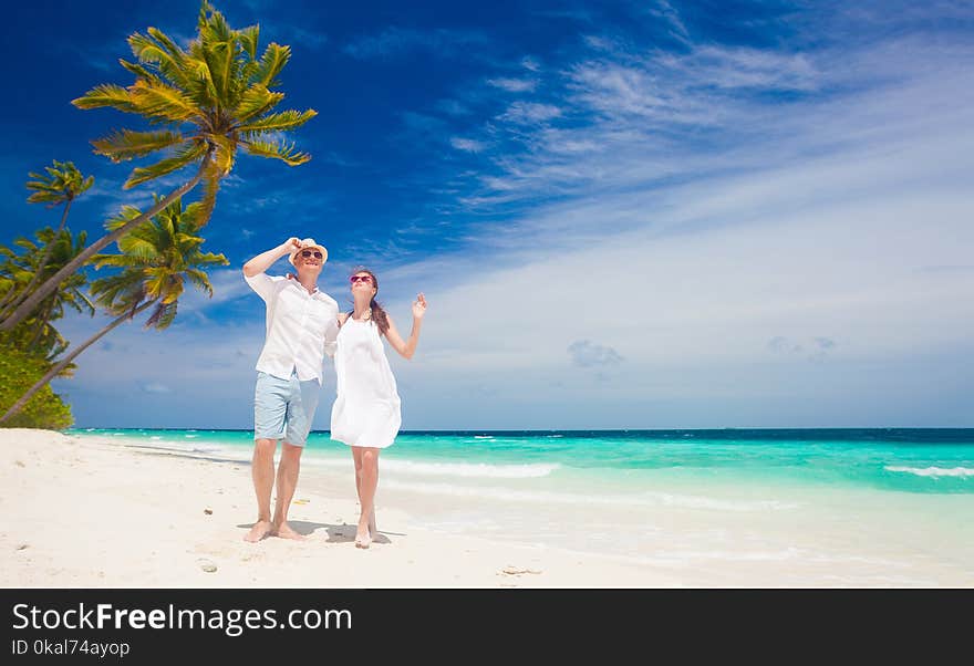 Happy young couple in white clothes walking by the beach. Maldives