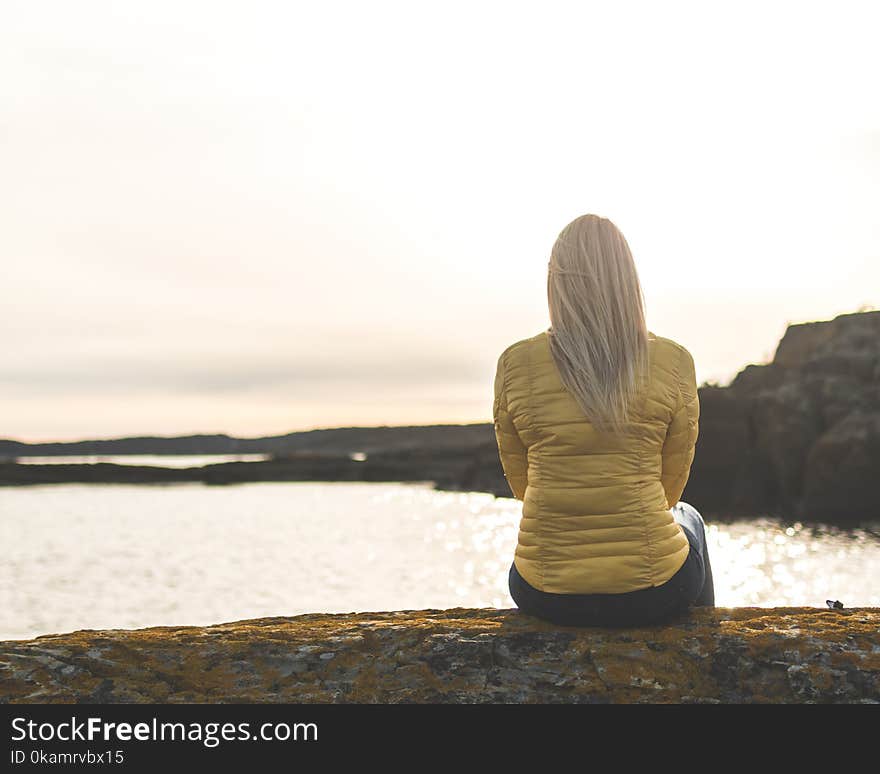 Woman Wearing Yellow Bubble Jacket Sitting in Front of Sea