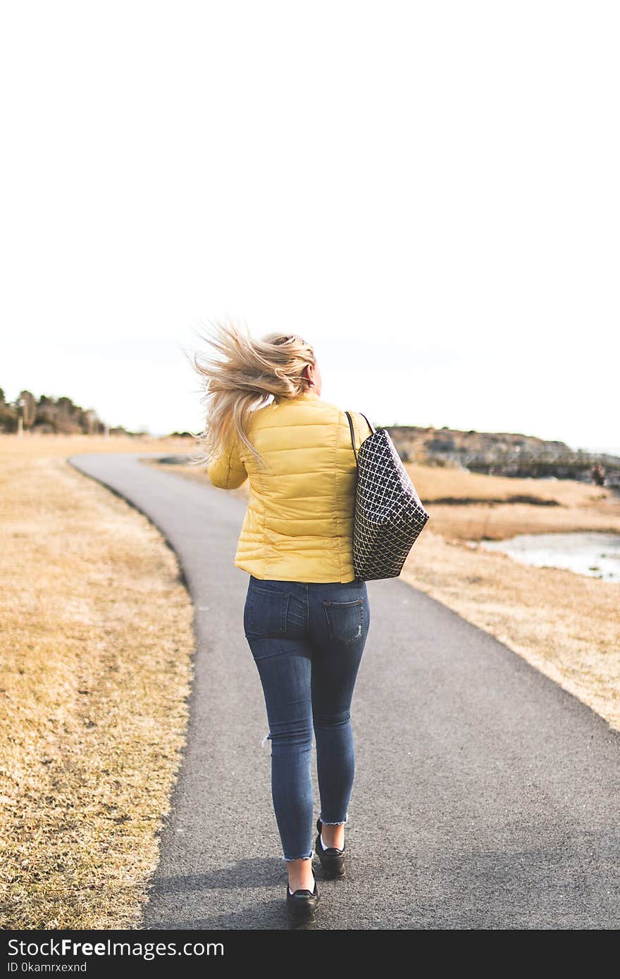 Woman Wears Yellow Bubble Jacket Walk Through Gray Asphalt Way