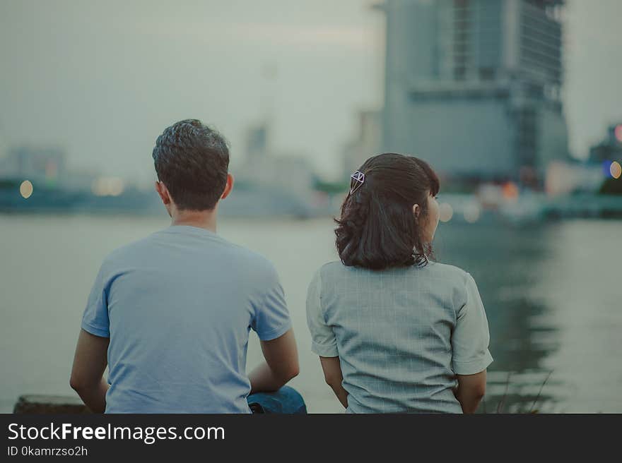 Selective Focus Photography of Man and Woman Watching Body of Water and Concrete Buildings