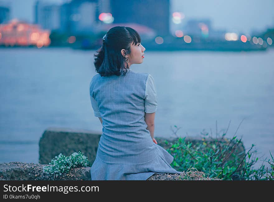 Woman Wearing Gray Dress Sitting Near Body of Water