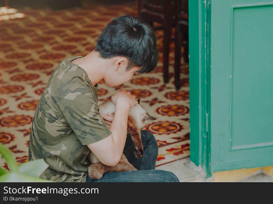 Photo of Boy Wearing Camouflage Shirt Holding a Cat