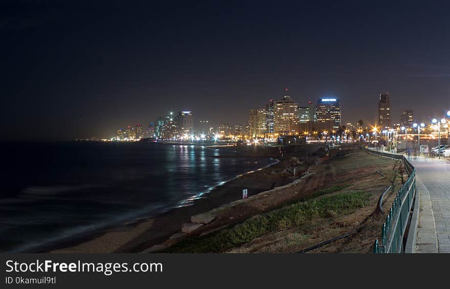 Grey Concrete Way Near Body of Water Leading to City during Nighttime