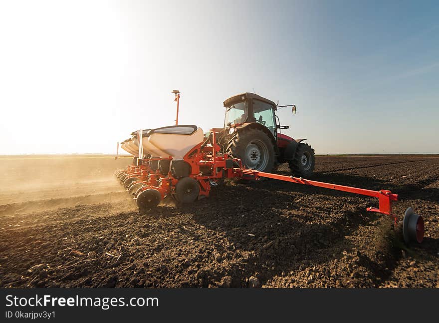 Farmer with tractor seeding - sowing crops at agricultural field