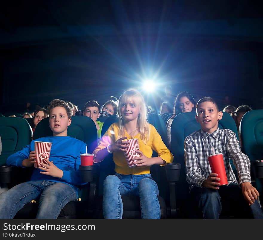 Best briends enjoying film in modern cinema, sitting in comfortable chairs. Youth eating popcorn and drinking fizzy drinks. Project light source. Concept of entertainment and cinematography. Best briends enjoying film in modern cinema, sitting in comfortable chairs. Youth eating popcorn and drinking fizzy drinks. Project light source. Concept of entertainment and cinematography.