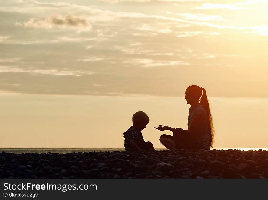 Mom and son playing on the beach with stones. Sunset time, silhouettes.